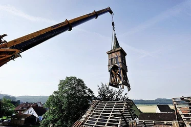 Abriss der alten Schule Ein Kran hebt einen baufälligen Schul-Glockenturm vor landschaftlicher Kulisse ab.