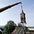 Abriss der alten Schule Ein Kran hebt einen baufälligen Schul-Glockenturm vor landschaftlicher Kulisse ab.
