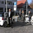 Elektro-Ladesäule Elektroauto, Fahrrad und Roller an einer Ladesäule auf einem gepflasterten Platz in der Stadt.