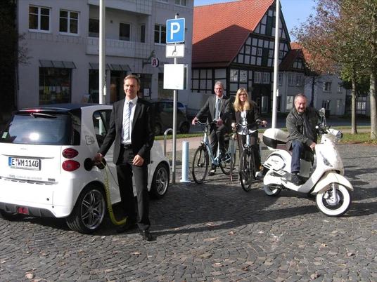Elektro-Ladesäule Elektroauto, Fahrrad und Roller an einer Ladesäule auf einem gepflasterten Platz in der Stadt.