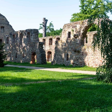 Remains of the walls of a former monastery with brick arches and a meadow surrounded by greenery.