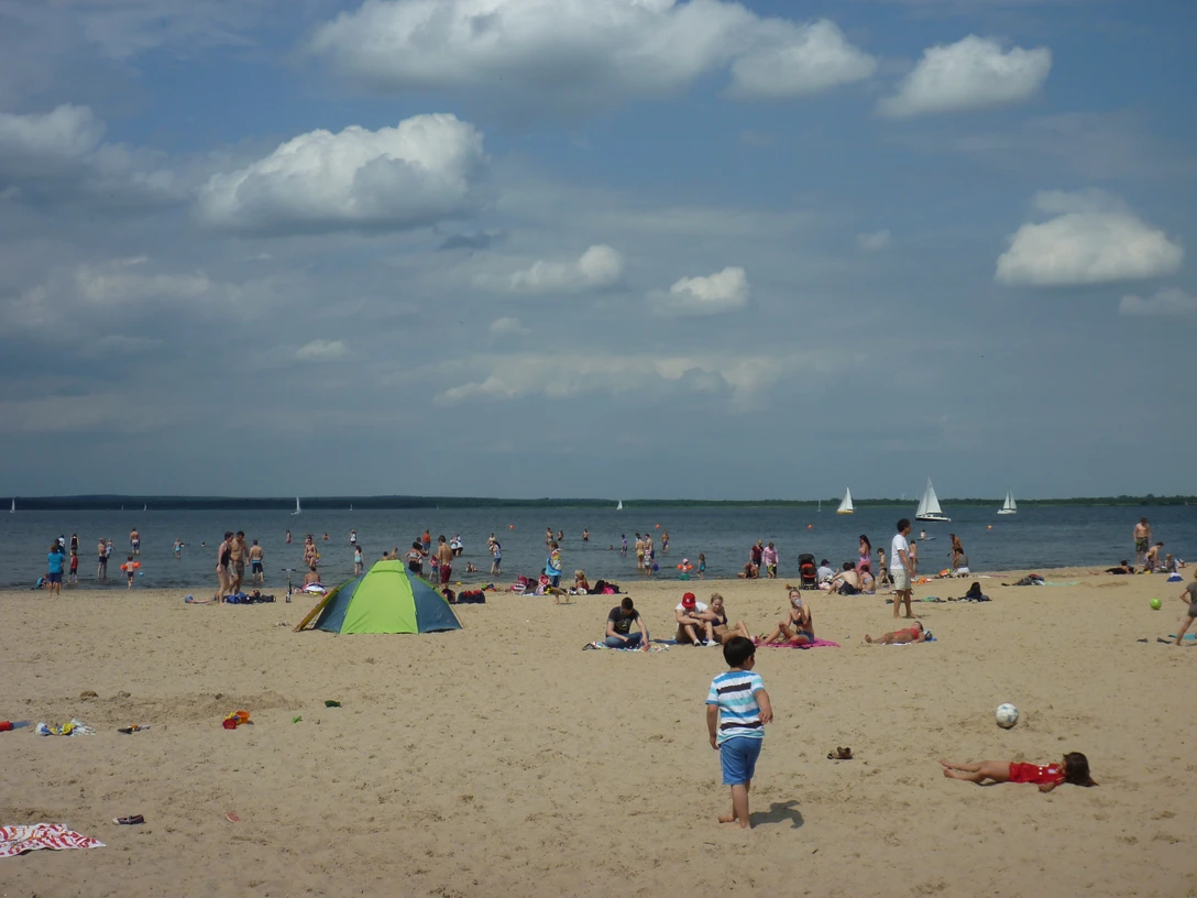 Badeinsel Steinhude Ein sonniger Strand voller Menschen mit bunten Badeanzügen und bunten Schirmen am Steinhuder Meer. Segelboote gleiten ruhig auf dem Wasser.A sunny beach full of people with colorful swimsuits and umbrellas on the Steinhuder Meer. Sailboats glide calmly on the water.En solrig strand fuld af mennesker med farverige badedragter og parasoller ved Steinhuder Meer. Sejlbåde glider roligt på vandet.Een zonnig strand vol mensen met kleurrijke zwemkleding en parasols aan het Steinhuder Meer. Zeilboten glijden rustig over het water.