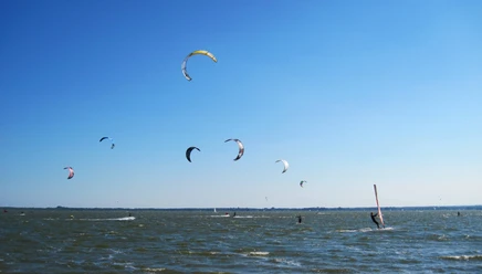 kiten-mardorf Kitesurfer gleiten an einem sonnigen Tag über das Wasser, prächtige Drachen tanzen am klaren Himmel.