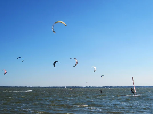 kiten-mardorf Kitesurfer gleiten an einem sonnigen Tag über das Wasser, prächtige Drachen tanzen am klaren Himmel.