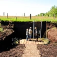 bodenstation-moor-kayhausen-gaestefuehrer Besucher begutachten eine Moorprofilwand in einer torfigen, naturnahen Landschaft.