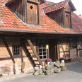 Historisches Fachwerkhaus mit rotem Ziegeldach, Holzverzierung und farbenfrohen Pflanzen im Vorgarten.