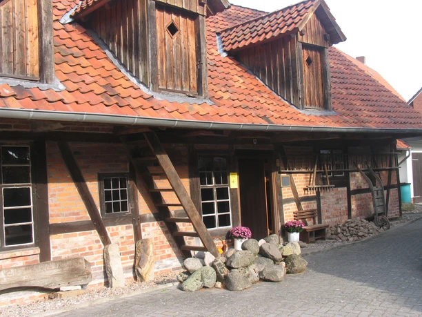 Historic half-timbered house with red tiled roof, wooden decorations and colorful plants in the front garden.