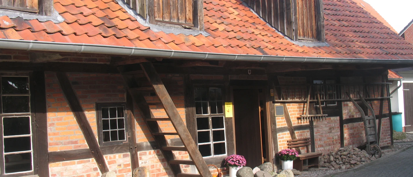 Kastenmangel in Steinhude Historisches Fachwerkhaus mit rotem Ziegeldach, Holzverzierung und farbenfrohen Pflanzen im Vorgarten.