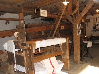 Kastenmangel Einsprengtisch Eine historische Webmaschine in einem traditionellen Bauernhausmuseum. Holzstruktur und alte Werkzeuge.