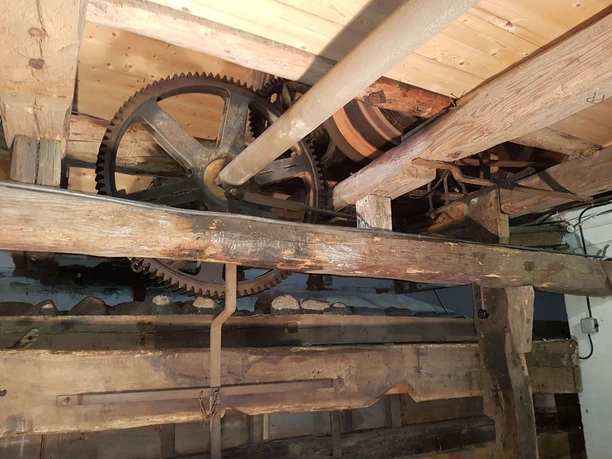 Alte Holzwassermühle mit rustikalen Zahnrädern und Balken, die historische Ingenieurskunst zeigt.