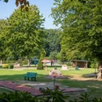 minigolf-uebersicht Ein weitläufiger Minigolfplatz, umgeben von Bäumen, mit bunten Sonnenschirmen und Bänken im Grünen.