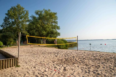 beach-volleyball Ein heißer Sommertag am See, ein Beachvolleyballfeld im Sand eingerahmt von grünen Bäumen.