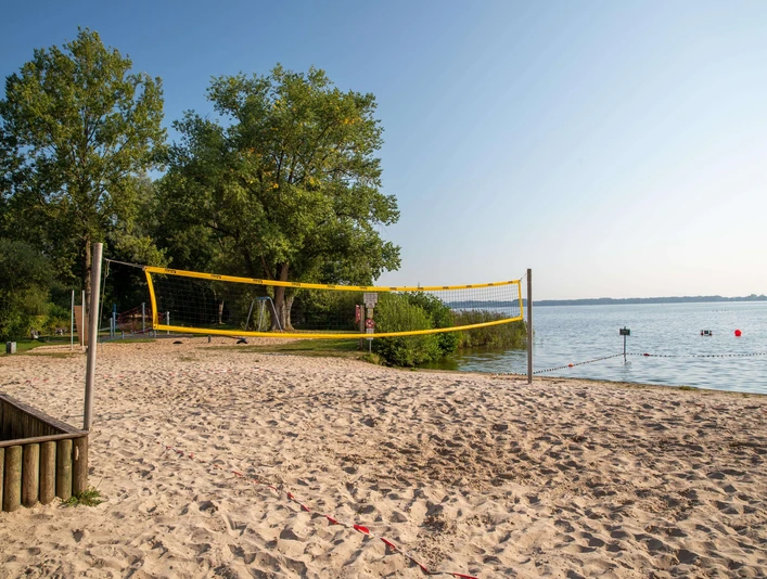 beach-volleyball Ein heißer Sommertag am See, ein Beachvolleyballfeld im Sand eingerahmt von grünen Bäumen.