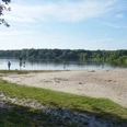 woldsee-strand-und-nichtschwimmerbereich Ein ruhiger Sandstrand am Woldsee mit klarem Wasser und umgebender grüner Natur lädt zum Entspannen ein.