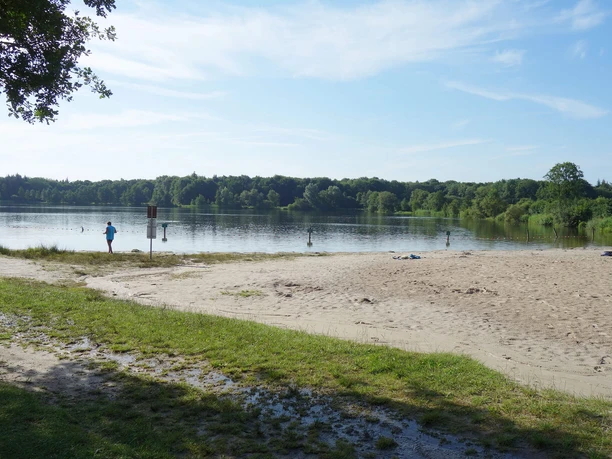 woldsee-strand-und-nichtschwimmerbereich Ein ruhiger Sandstrand am Woldsee mit klarem Wasser und umgebender grüner Natur lädt zum Entspannen ein.