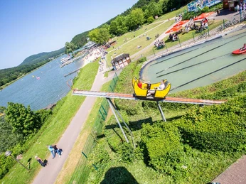 Familienfreundlicher Freizeitpark mit See, Wasserrutsche und Bootsfahrten umgeben von grüner Landschaft.