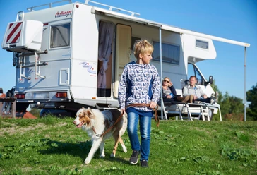 Camping in Dithmarschen (Symbolbild) Junge führt Hund vor Wohnmobil und Familie