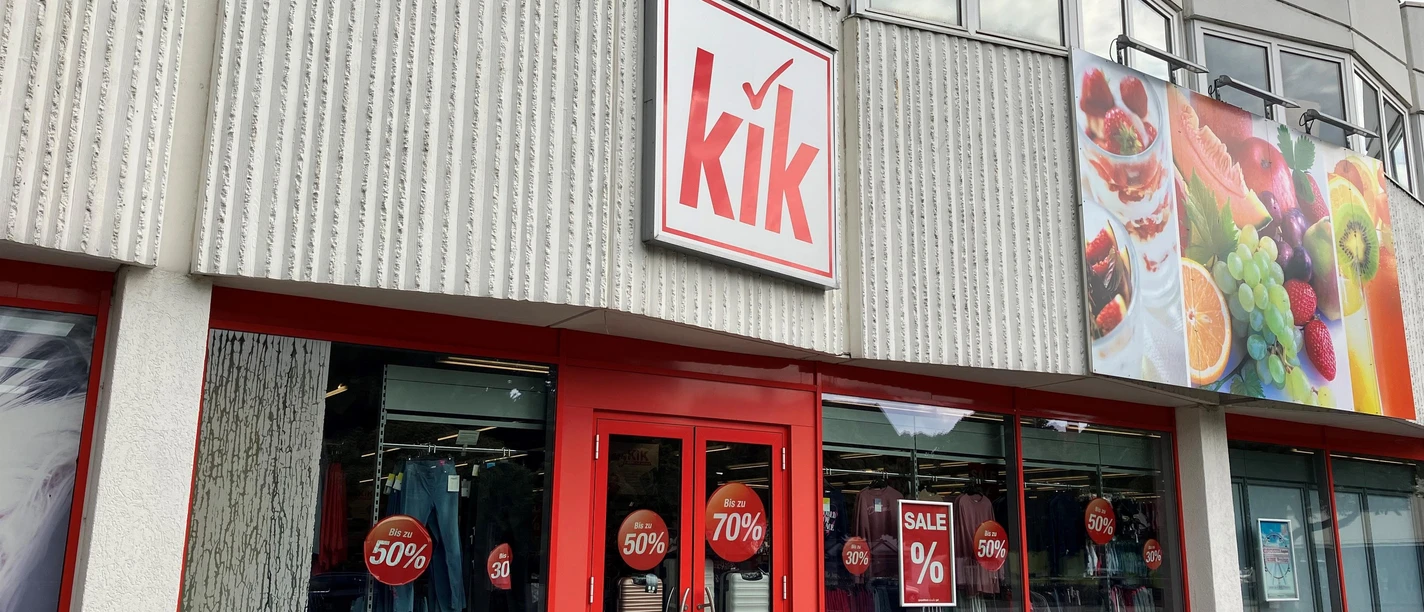 KiK-Filiale mit rotem Eingang, Schaufenstern und Sale-Plakaten an heller Fassade