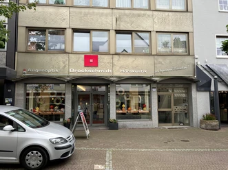 Schaufenster von Brockschmidt Augenoptik und Hörakustik mit Hauseingang und geparktem Auto