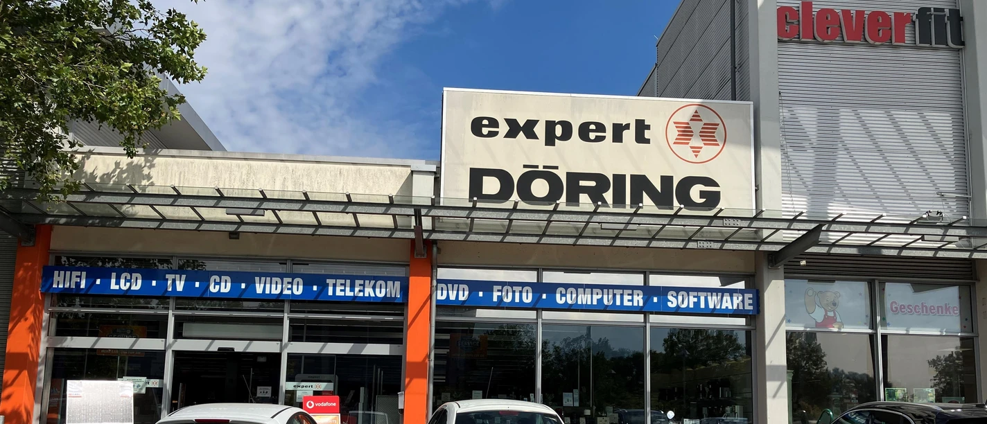 Außenansicht von Expert Döring mit Schaufenstern, Firmenschild und parkenden Autos