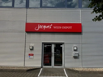Eingang von Jacques' Wein-Depot mit rotem Schild an einer silbernen Metallfassade