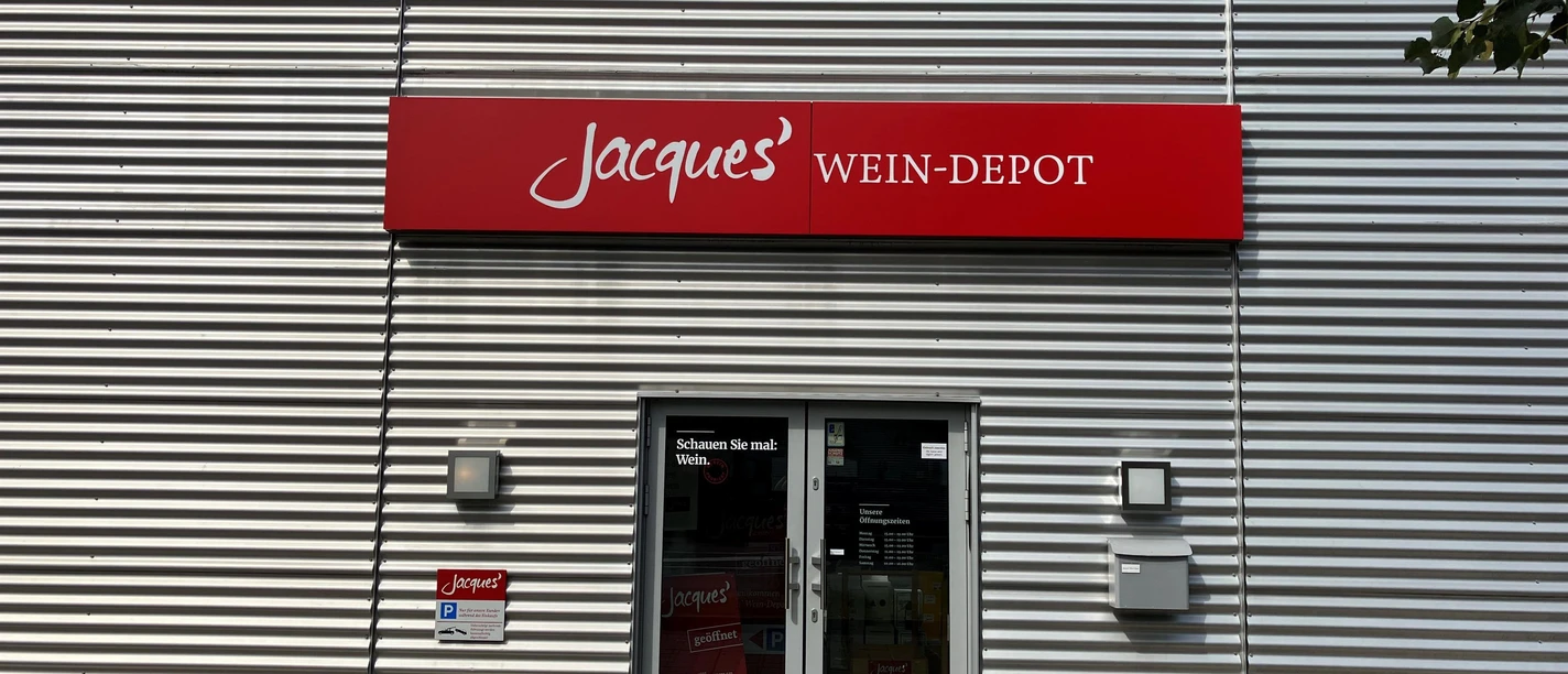Eingang von Jacques' Wein-Depot mit rotem Schild an einer silbernen Metallfassade