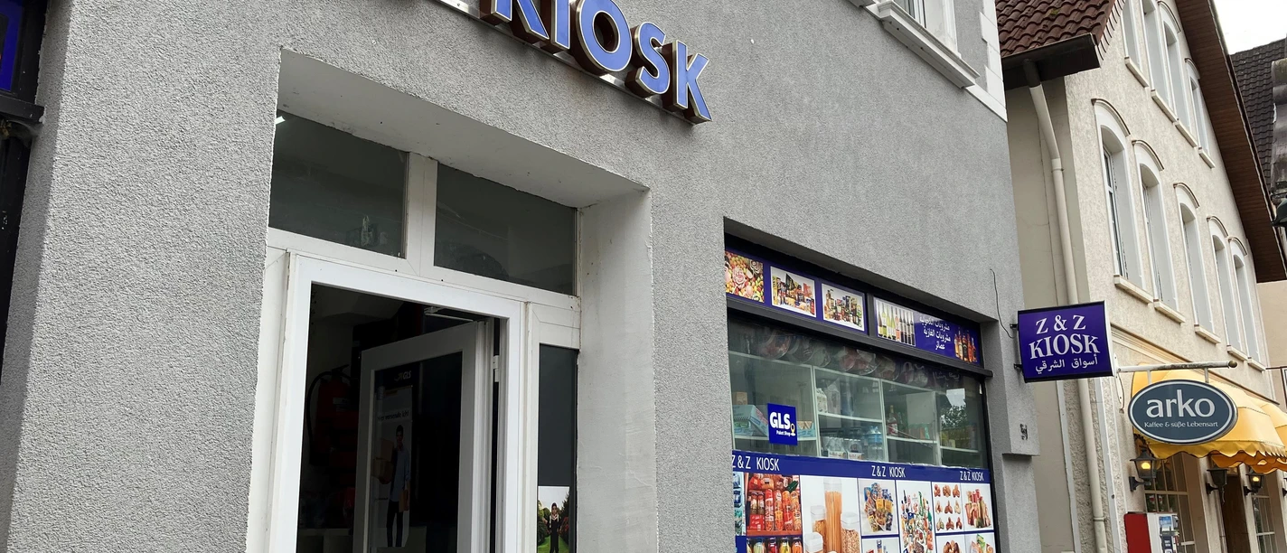 Graue Hausfassade des Z & Z Kiosk mit blauem Schriftzug und Schaufenster