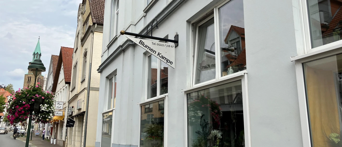 Außenansicht von Blumen Kampe mit Schaufenstern, Ausleger und Blumenschmuck am Gehweg