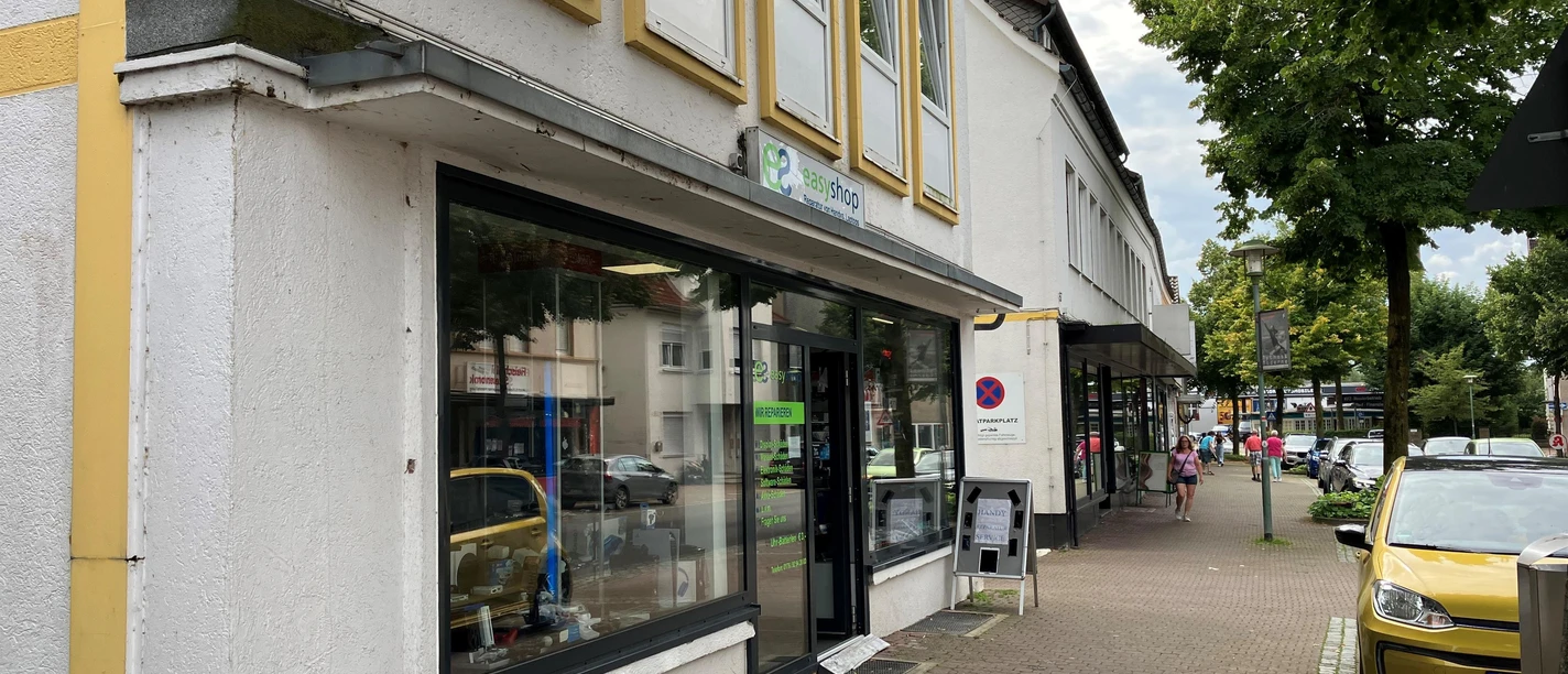 Außenansicht des Easy Shop mit Schaufenstern an einer begrünten Geschäftsstraße