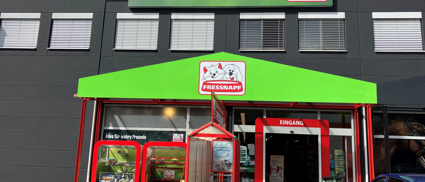 Fressnapf-Filiale mit grünem Vordach, Eingang und Einkaufswagen vor dunkler Fassade