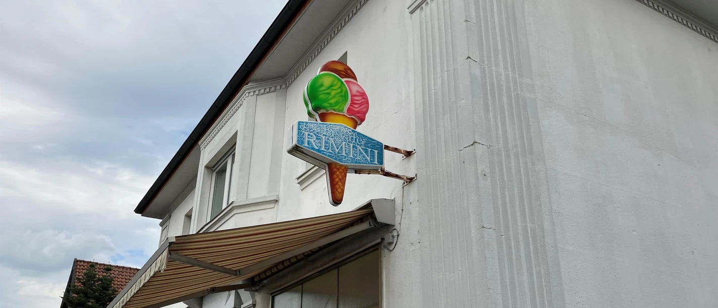 Fassadenschild des Eiscafé Rimini mit bunter Eistüte an weißer Hauswand