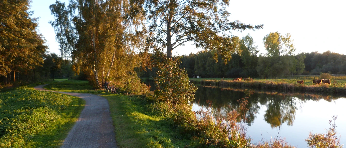 A quiet path leads along the Hagenburg Canal with trees and a peaceful water surface.