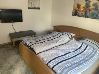 Schlafzimmer Ein Doppelbett mit gestreifter Bettwäsche in einem schlichten, hellen Schlafzimmer mit TV an der Wand.
