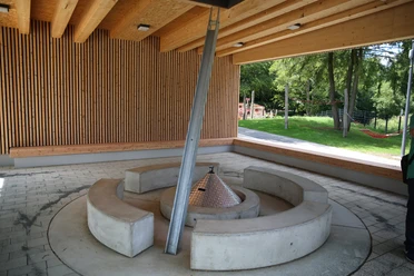 überdachter Grillplatz im Wiehlpark Überdachte Feuerstelle mit moderner Architektur, umgeben von Bänken in einer offenen Holzkonstruktion.