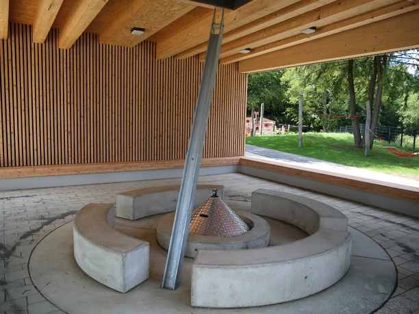 überdachter Grillplatz im Wiehlpark Überdachte Feuerstelle mit moderner Architektur, umgeben von Bänken in einer offenen Holzkonstruktion.