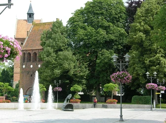 st-johannes-kirche Springbrunnen am Marktplatz Bad Zwischenahn vor dem Backsteinturm der St. Johannes-Kirche.