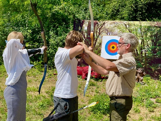 Bogenschule in Erkrath Menschen üben in einem sonnigen, von Bäumen umgebenen Bogenschießbereich das Spanntechnik verbessern.