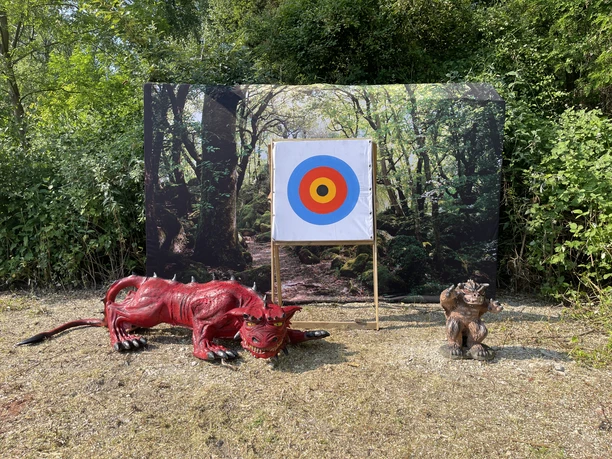 Bogenschule in Erkrath Eine Waldlichtung mit einer Zielscheibe, umgeben von Plastiktiere eines Drachen und eines Affen.