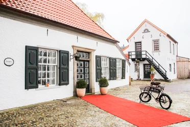 Alte Drostei in Papenburg Historisches Backsteinhaus mit roten Dachziegeln, grün-weißen Fensterläden und rotem Teppichweg.