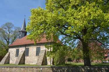 Kirche Münchehagen Historische Kirche mit rotem Ziegeldach und markantem Turm, umgeben von altem Baumbestand.