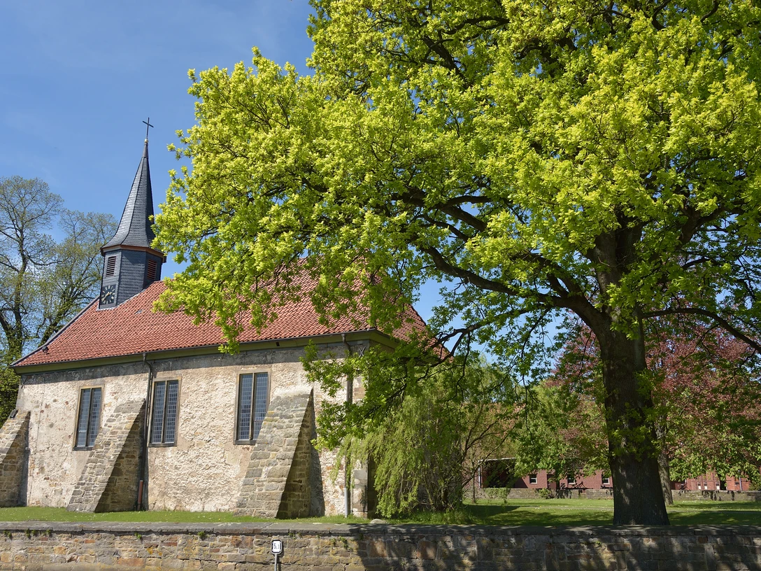 Kirche Münchehagen Historische Kirche mit rotem Ziegeldach und markantem Turm, umgeben von altem Baumbestand.