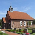 Fachwerk-Kapelle Winzlar Fachwerk-Kapelle mit rotem Ziegeldach und Glockenturm, umgeben von gepflegtem Garten und Grabsteinen.