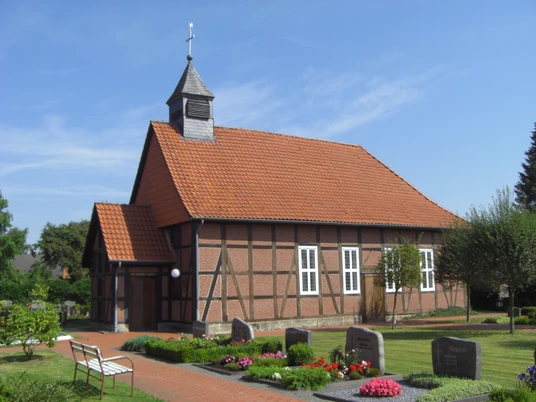 Fachwerk-Kapelle Winzlar Fachwerk-Kapelle mit rotem Ziegeldach und Glockenturm, umgeben von gepflegtem Garten und Grabsteinen.
