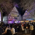 Historische Fachwerkhäuser erleuchten im Abendlicht bei einem belebten Weihnachtsmarkt in Beverungen.