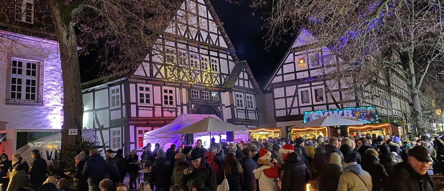 Historische Fachwerkhäuser erleuchten im Abendlicht bei einem belebten Weihnachtsmarkt in Beverungen.