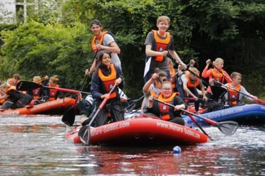 Stand Up Paddling Jugendliche in orangen Rettungswesten paddeln auf großen roten SUP-Boards auf einem Fluss.