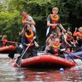 Stand Up Paddling Jugendliche in orangen Rettungswesten paddeln auf großen roten SUP-Boards auf einem Fluss.
