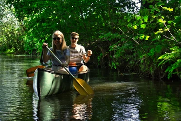 Zwei Menschen in einem Kanu genießen die Fahrt auf dem von Bäumen gesäumten Fluss.