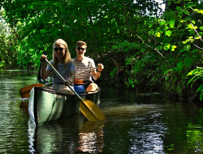 Zwei Menschen in einem Kanu genießen die Fahrt auf dem von Bäumen gesäumten Fluss.