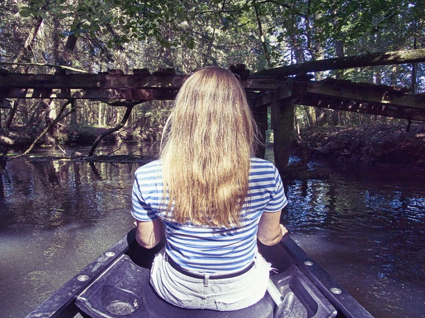 Einfach mal treiben lassen Eine junge Frau sitzt in einem Kanu, treibt auf einem ruhigen Fluss unter einer alten Holzbrücke. Das umgebende dichte Grün vermittelt Ruhe und Gelassenheit.